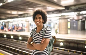 Imagem de um homem jovem sorrindo enquanto aguarda o trem em uma estação de metrô para ilustrar matéria sobre Linha 8-Diamante