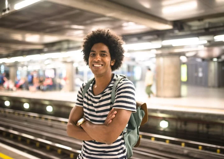 Imagem de um homem jovem sorrindo enquanto aguarda o trem em uma estação de metrô para ilustrar matéria sobre Linha 8-Diamante