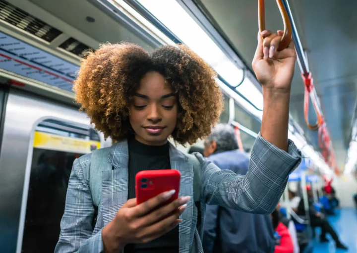 Imagem de uma mulher negra em pé em um metrô segurando na barra de segurança enquanto olha para a tela do celular para ilustrar matéria sobre a Linha Verde do metrô de SP