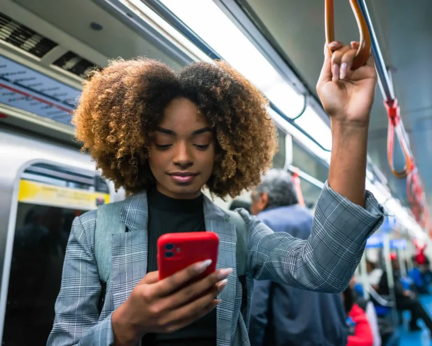Imagem de uma mulher negra em pé em um metrô segurando na barra de segurança enquanto olha para a tela do celular para ilustrar matéria sobre a Linha Verde do metrô de SP