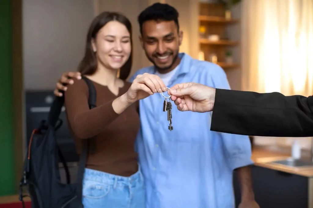 Imagem de um casal sorridente recebendo um conjunto de chaves de uma pessoa de terno para ilustrar matéria sobre o que é contrato de permuta de imóveis.