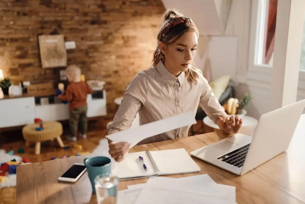 Imagem de uma mulher trabalhando em uma mesa com um notebook e papéis, parecendo concentrada, para ilustrar matéria sobre o que é permuta de imóveis com torna. 