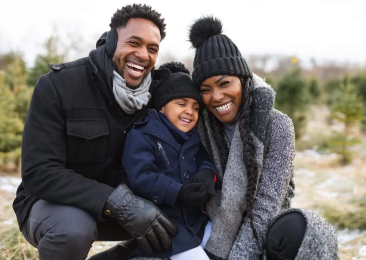 Imagem de uma família formada por um homem, uma mulher e uma criança sorrindo e agasalhada com touca, cachecol e luva para ilustrar matéria sobre qual a cidade mais fria do Nordeste