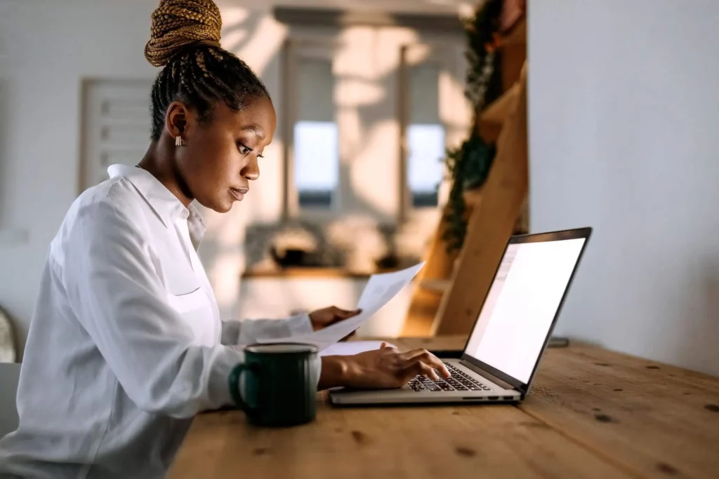 Imagem de uma mulher sentada e digitando em um notebook para ilustrar matéria sobre quem não tem carteira assinada consegue financiar um imóvel?