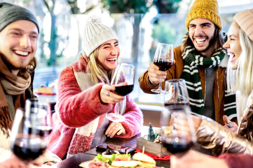 Imagem de um grupo de quatro amigos agasalhados sorrindo enquanto brindam com taças de vinho para ilustrar matéria sobre as regiões mais frias do Rio Grande do Sul