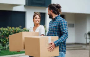Imagem de um casal formado por um homem e uma mulher caminhando em frente a uma casa com caixas de papelão nas mãos para ilustrar matéria sobre Triângulo Mineiro