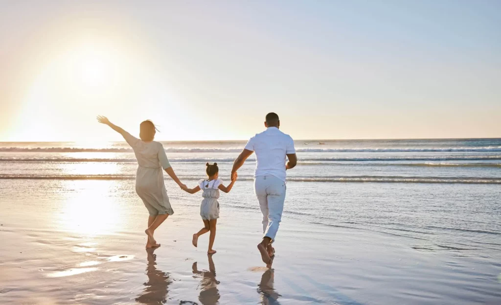 Imagem de uma família composta por um homem, uma mulher e uma criança correndo descalços em direção ao mar para ilustrar matéria sobre a cidade qua mais cresce em Santa Catarina