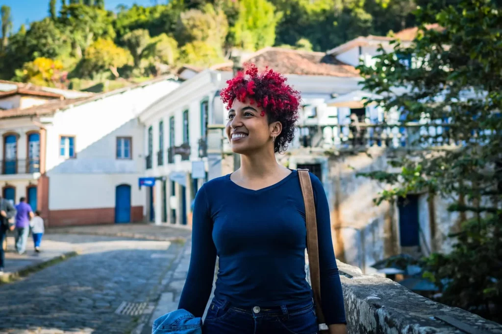 Imagem de jovem mulher com cabelo curto e rosa, com uma bolsa no ombro, andando por um bairro, para ilustrar matéria sobre as cidades que mais cresceram em Minas Gerais 