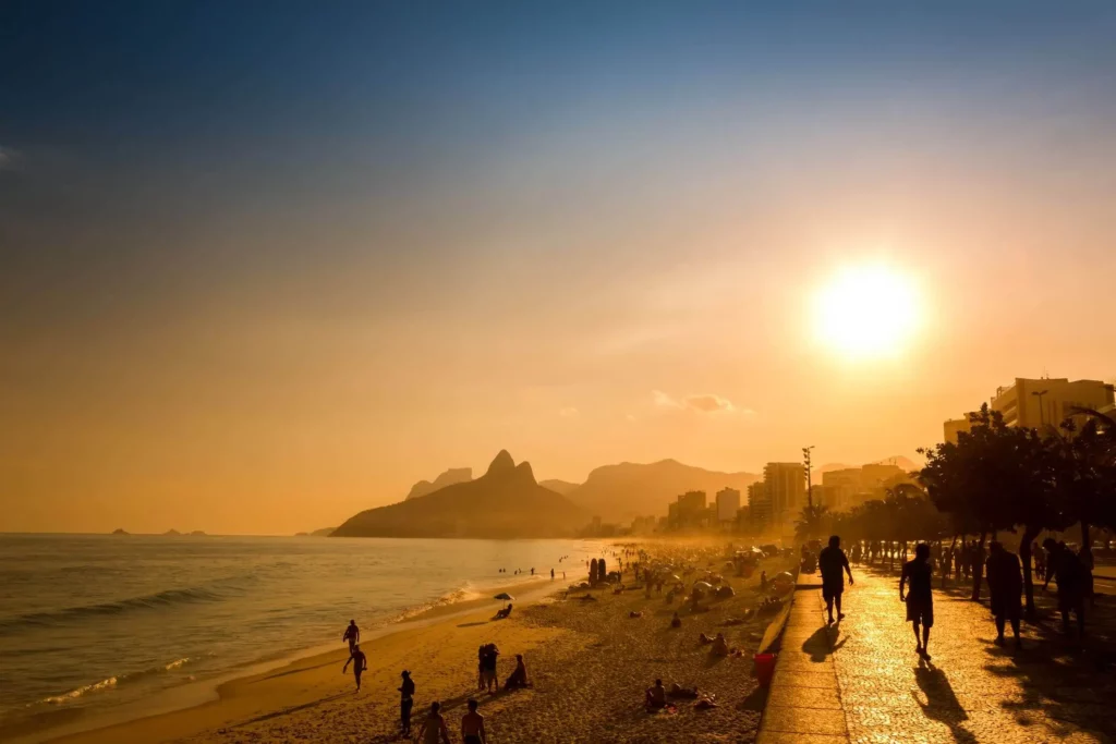 Imagem panorâmica de pessoas aproveitando a praia e caminhando na orla durante o pôr do sol para ilustrar matéria sobre qual o bairro mais quente do Rio de Janeiro