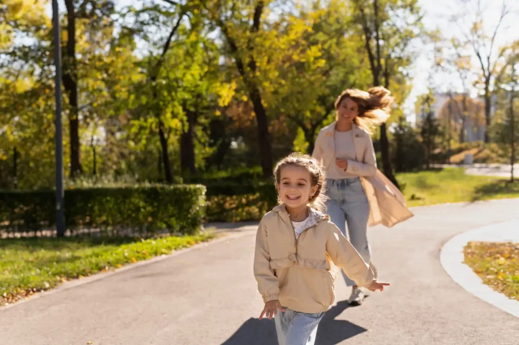 Imagem de uma criança sorridente correndo na frente da mãe que vem logo atrás em uma pista de caminhada cercada por um parque para ilustrar matéria sobre a cidade do Brasil com o melhor saneamento básico