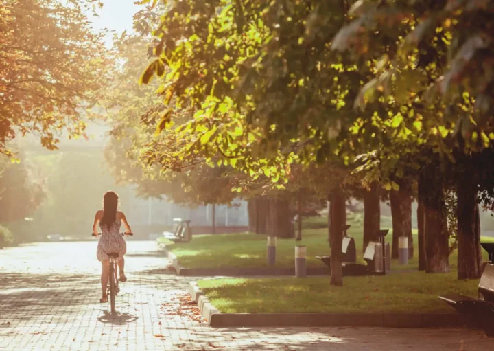 magem de uma mulher andando de bicicleta em uma ciclovia em meio às árvores em um parque no fim da tarde para ilustrar matéria sobre parques na Zona Leste de SP