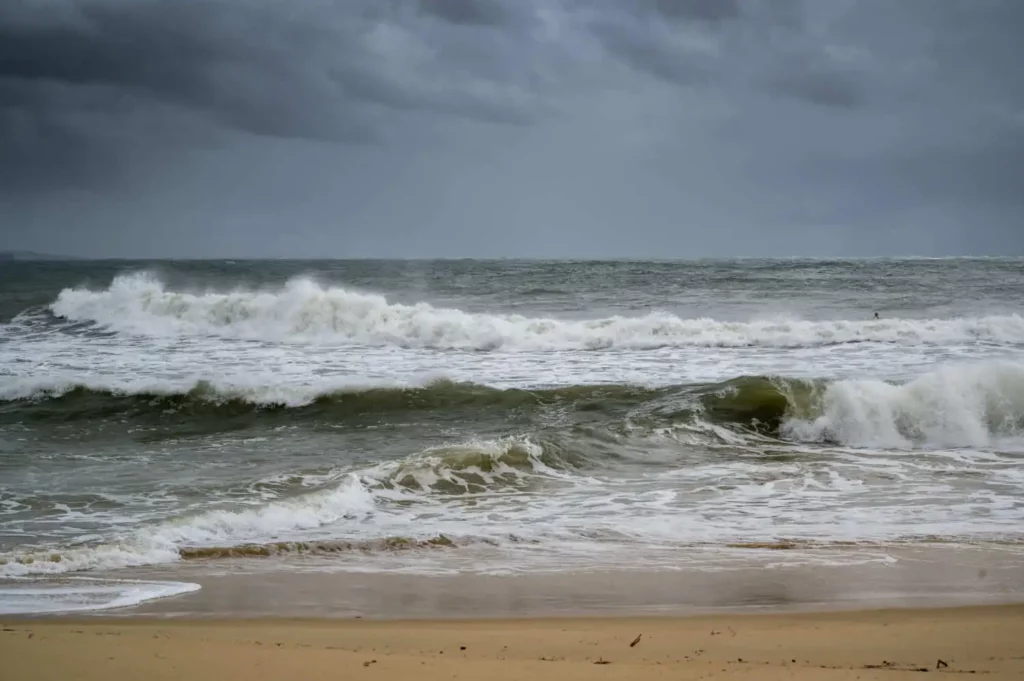 Imagem de uma praia vazia com ondas fortes e nuvens escuras e carregadas para ilustrar matéria sobre qual é o mês que mais chove em Santa Catarina