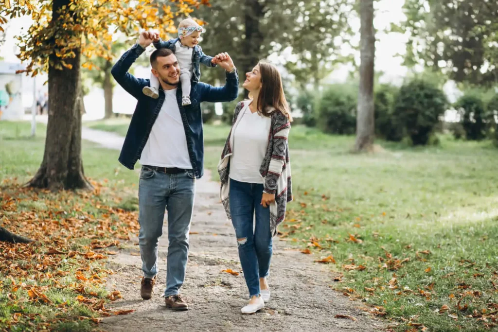 Imagem de casal composto por um homem com uma criança pequena nas costas e uma mulher andando em um parque urbano para ilustrar matéria sobre qual o bairro mais populoso do RJ