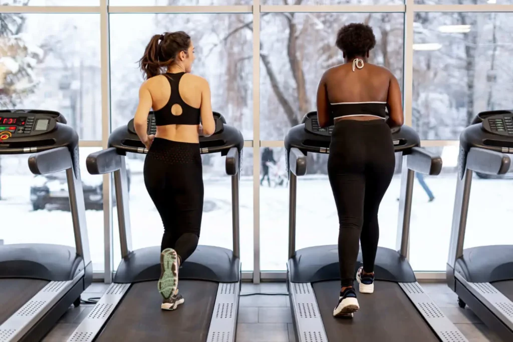 Imagem de duas mulheres correndo em esteiras uma ao lado da outra para ilustrar matéria sobre condomínio com academia