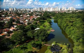 Imagem da vista aérea do Jardim Botânico de Goiânia mostra lago, vegetação, casas ao redor e prédios ao fundo em um dia de céu azul para ilustrar matéria sobre os bairros de Goiânia.