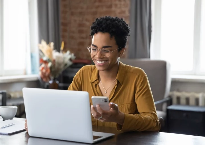 Foto que ilustra matéria sobre tecnologia no mercado imobiliário mostra uma mulher olhando a tela de um laptop enquanto segura um celular (Foto: Shutterstock)