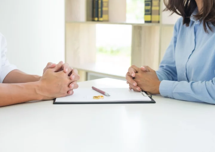 Foto que ilustra matéria sobre usucapião familiar mostra um contrato de divórcio em cima de uma mesa com duas alianças e uma caneta sobre ele. De cada lado da mesa estão um homem e uma mulher (Foto: Shutterstock)