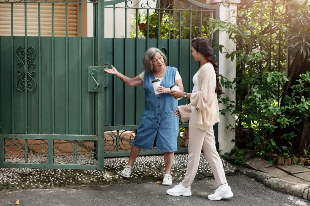 Imagem de uma jovem com café na mão conversando com uma senhora em frente a um portão verde para ilustrar matéria sobre converse com moradores