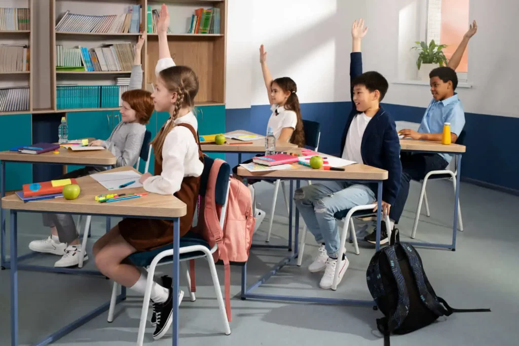 Imagem de alunos mais velhos com os braços levantados, sentados nas carteiras escolares em sala de aula para ilustrar matéria sobre escolas mais buscadas em Nova Iguaçu