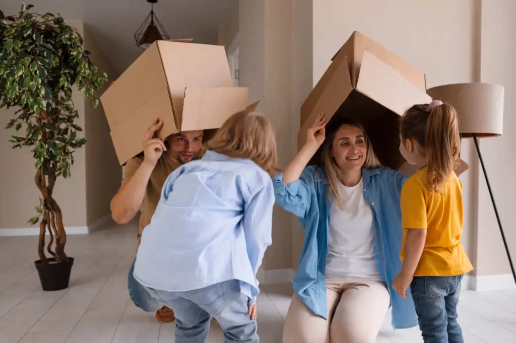 Imagem de uma família composta por um homem, uma mulher e duas crianças brincando com caixas de papelão dentro de uma casa para ilustrar matéria sobre as escolas em Mesquita, no Rio de Janeiro