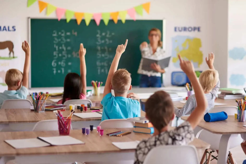 Imagem de uma sala de aula cheia com alunos de mãos levantadas para tirar dúvida para ilustrar matéria sobre as escolas particulares na cidade de Mesquita