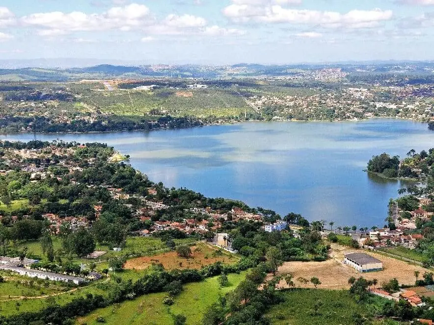 Imagem de lagoa cercada por vegetação e casas em um dia de céu azul na cidade de Lagoa Santa, em Minas Gerais