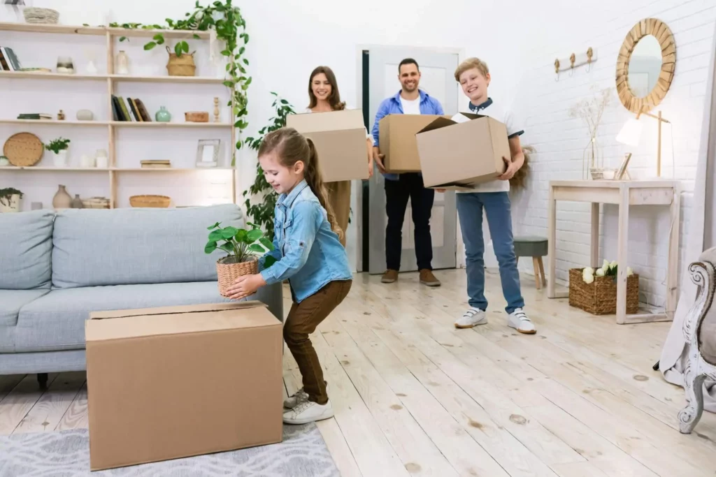  Imagem de uma família composta por um homem, uma mulher e duas crianças entrando na sala de um imóvel mobiliado com algumas caixas de papelão nas mãos para ilustrar matéria sobre o melhor bairro de Mesquita