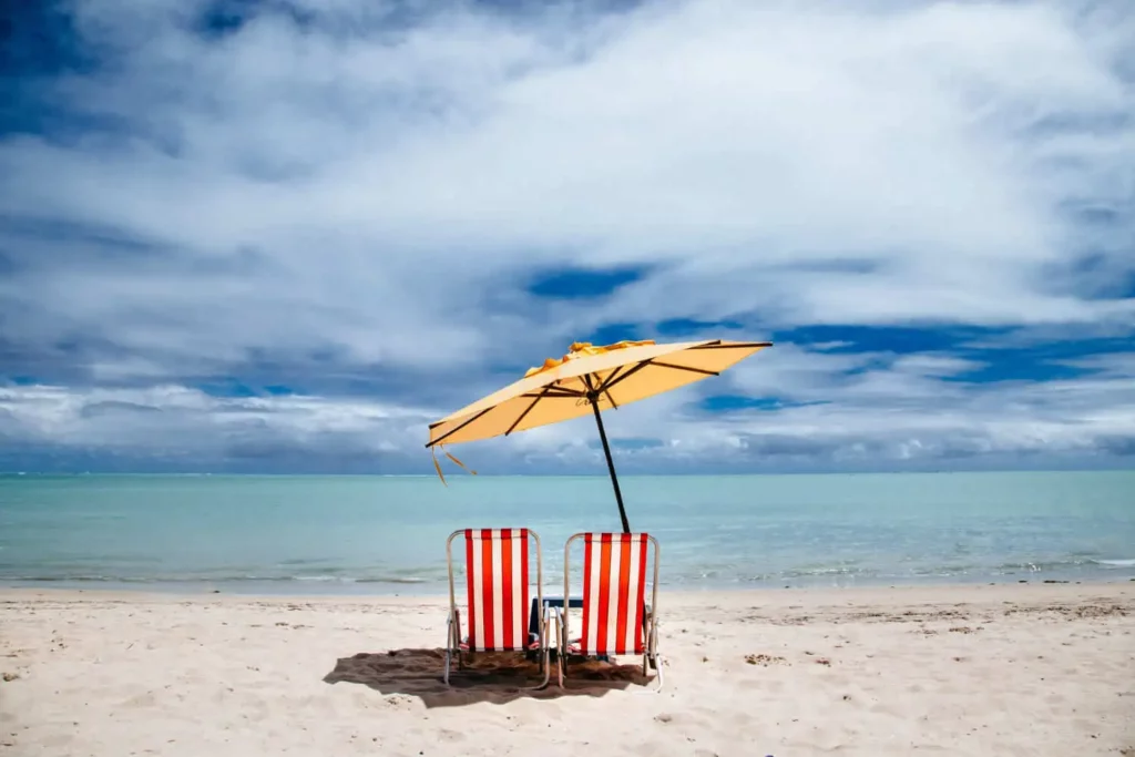 Imagem de duas cadeiras de praia debaixo de um guarda-sol na areia de frente ao mar para ilustrar matéria sobre qual é o melhor posto da praia da Barra da Tijuca