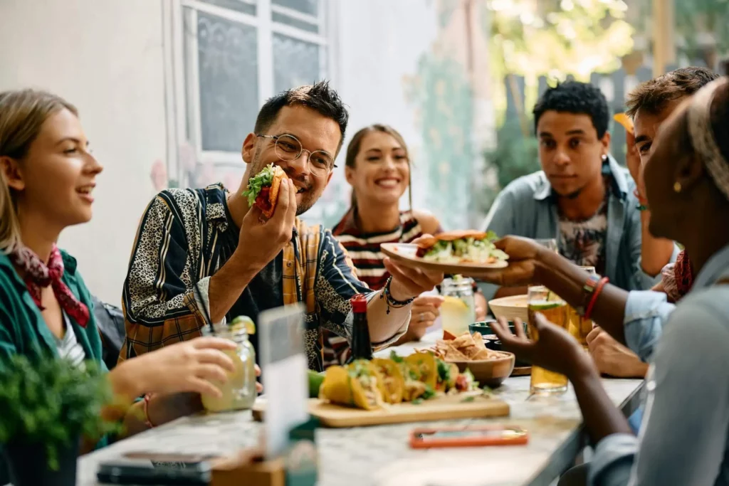 Imagem de amigos sentados ao redor de uma mesa sorrindo enquanto comem tacos e outras comidas de origem mexicana para ilustrar matéria sobre restaurantes acessíveis em São Paulo