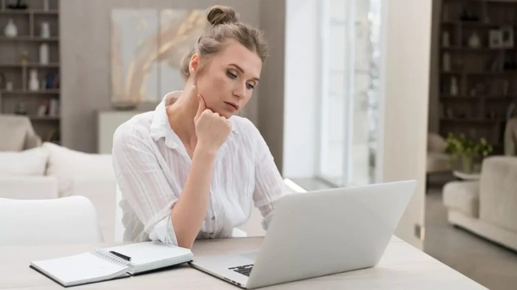 Imagem de uma mulher sentada na mesa de casa olhando pensativa para a tela de um notebook que está em cima da mesa para ilustrar matéria sobre ação de despejo em uma denúncia vazia