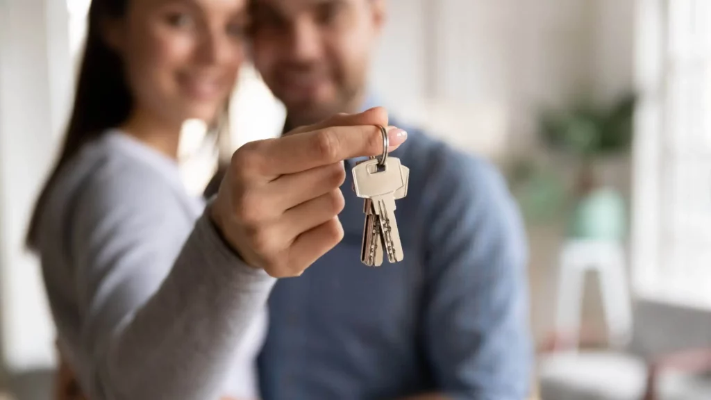 Imagem de uma mulher segurando a chave de um imóvel enquanto abraça seu parceiro para ilustrar matéria sobre como pagar financiamento imobiliário