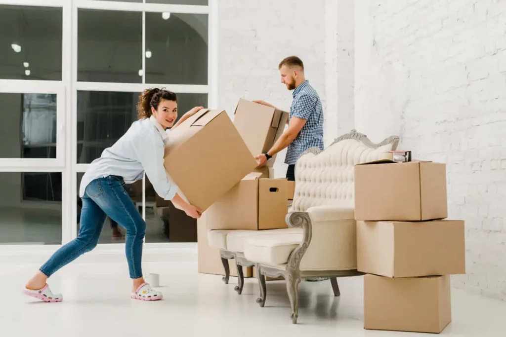 Imagem de uma mulher e um homem carregando caixas de mudança em um cômodo vazio para ilustrar matéria sobre como se preparar para comprar uma casa sem entrada