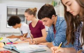 Imagem de quatro estudantes adolescentes sentados em uma mesa comprida com livros e cadernos enquanto estudam concentrados para ilustrar matéria sobre as escolas em Belford Roxo, no Rio de Janeiro