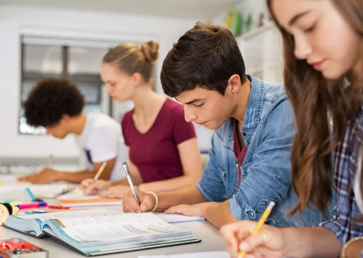 Imagem de quatro estudantes adolescentes sentados em uma mesa comprida com livros e cadernos enquanto estudam concentrados para ilustrar matéria sobre as escolas em Belford Roxo, no Rio de Janeiro