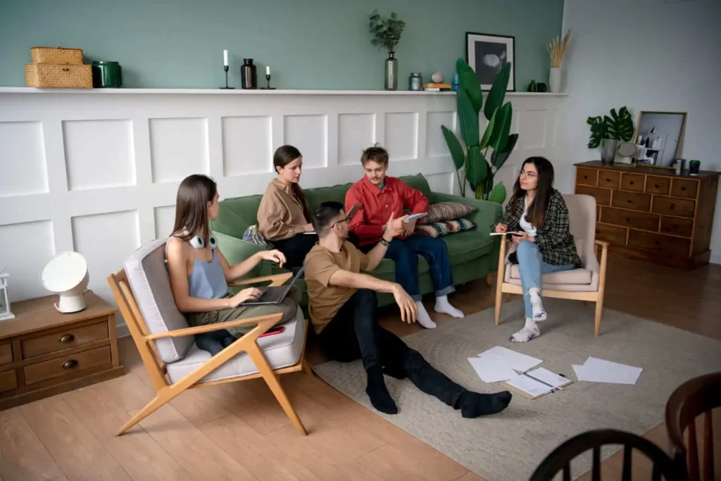 Imagem de três mulheres e dois homens sentados no sofá, cadeiras e no chão de uma sala enquanto conversam para ilustrar matéria sobre se herdeiro pode impedir a venda de imóvel