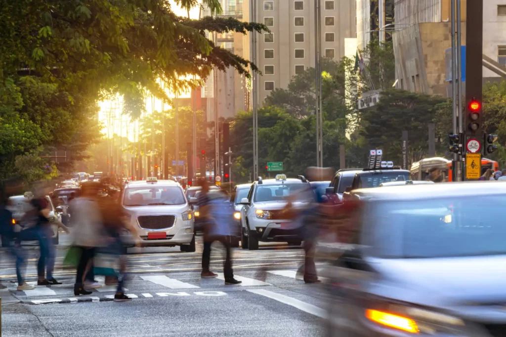 Imagem de pessoas e carros atravessando a Avenida Paulista para ilustrar matéria sobre os melhores bairros para investir em São Paulo