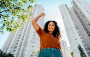 Imagem de uma mulher comemorando ao ar livre em frente a um empreendimento imobiliário para ilustrar matéria sobre os melhores bairros para investir em SP