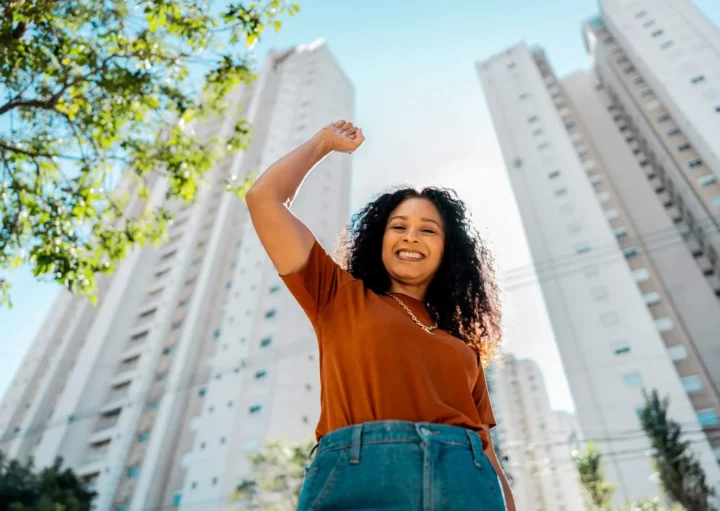 Imagem de uma mulher comemorando ao ar livre em frente a um empreendimento imobiliário para ilustrar matéria sobre os melhores bairros para investir em SP