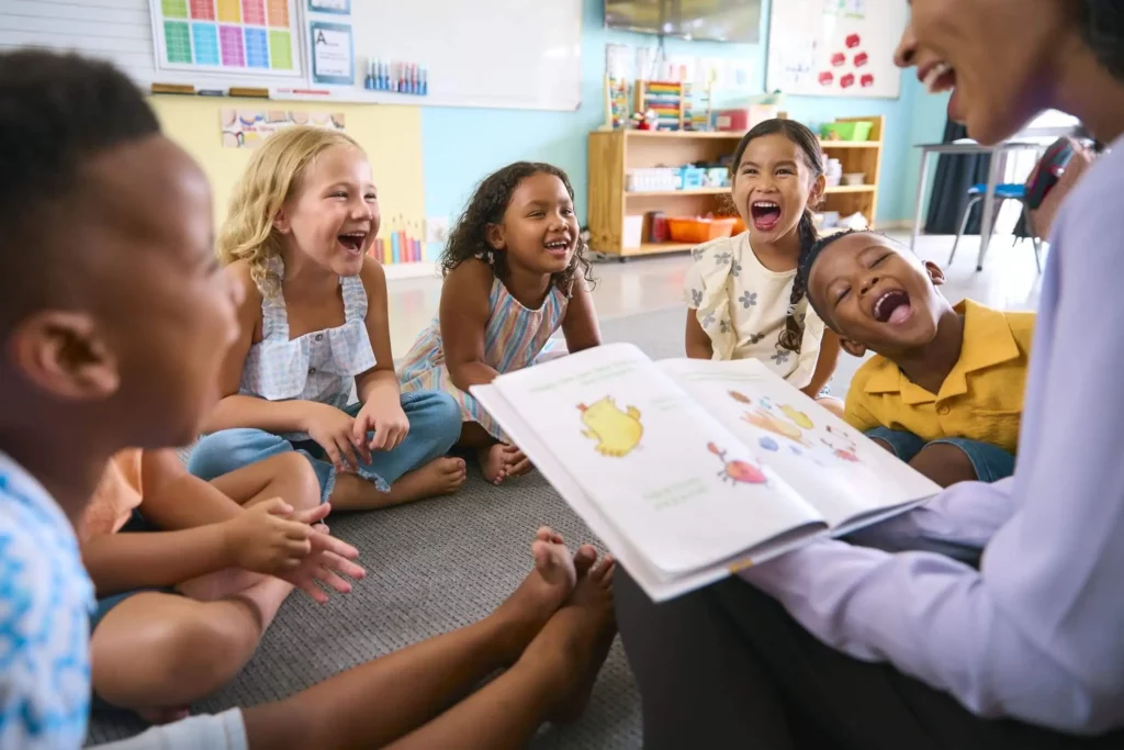 Imagem de uma turma de educação infantil onde várias crianças estão sentadas em círculo olhando para a professora que está com um livro na mão para ilustrar matéria sobre as melhores escolas particulares em Duque de Caxias