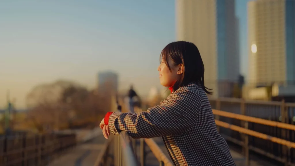 Imagem de uma mulher encostada na varanda de um prédio ao ar livre enquanto observa a vista da cidade durante o pôr do sol para ilustrar matéria sobre quais são as cidades do futuro