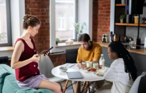 Imagem de uma mulher sentada na almofada de um sofá enquanto um homem e uma mulher estão sentados em frente em uma mesa com um notebook e vasilha em cima dentro de um imóvel para ilustrar matéria sobre se um herdeiro pode impedir a venda de um imóvel