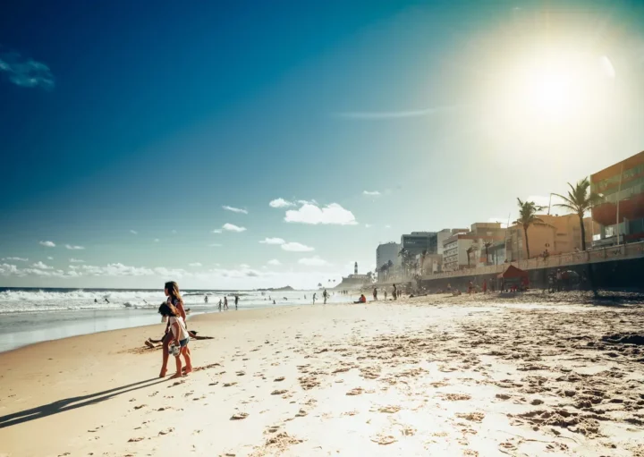 Foto que ilustra matéria sobre o que fazer em Salvador com crianças mostra duas meninas na areia de uma das praias da cidade em um dia de céu azul com poucas nuvens (Foto: Getty Images)