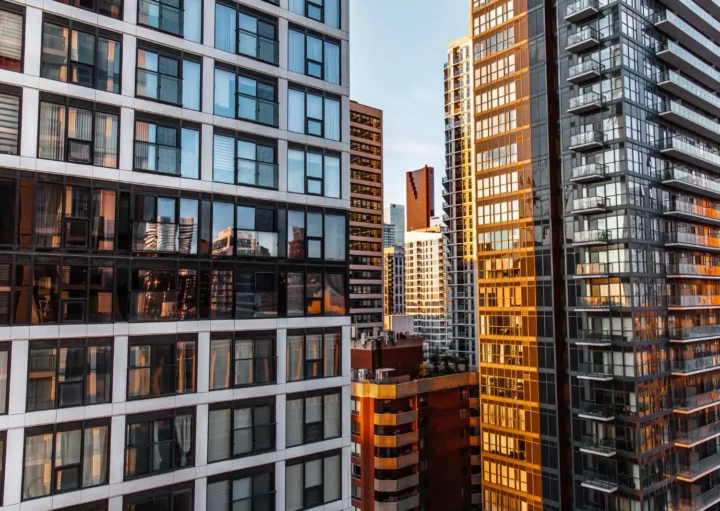 Imagem panorâmica de prédios altos de vidro e modernos com luz do pôr do sol refletida para ilustrar matéria sobre apartamento próprio