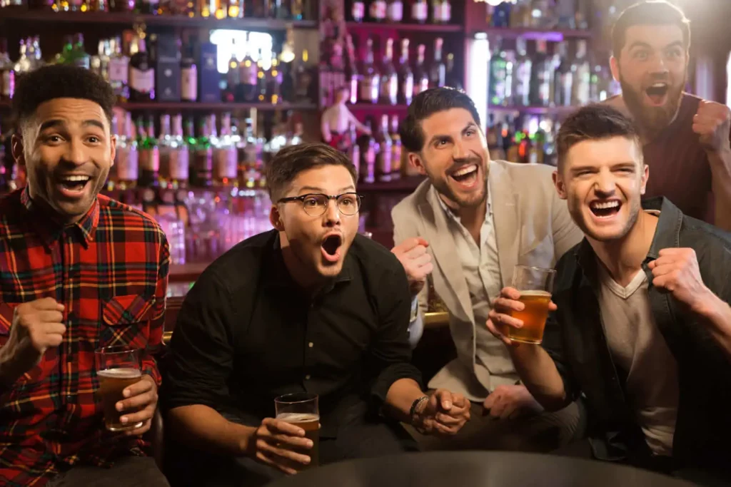 Imagem de amigos torcendo durante um jogo ao redor de uma mesa de bar para ilustrar matéria sobre bar com TV