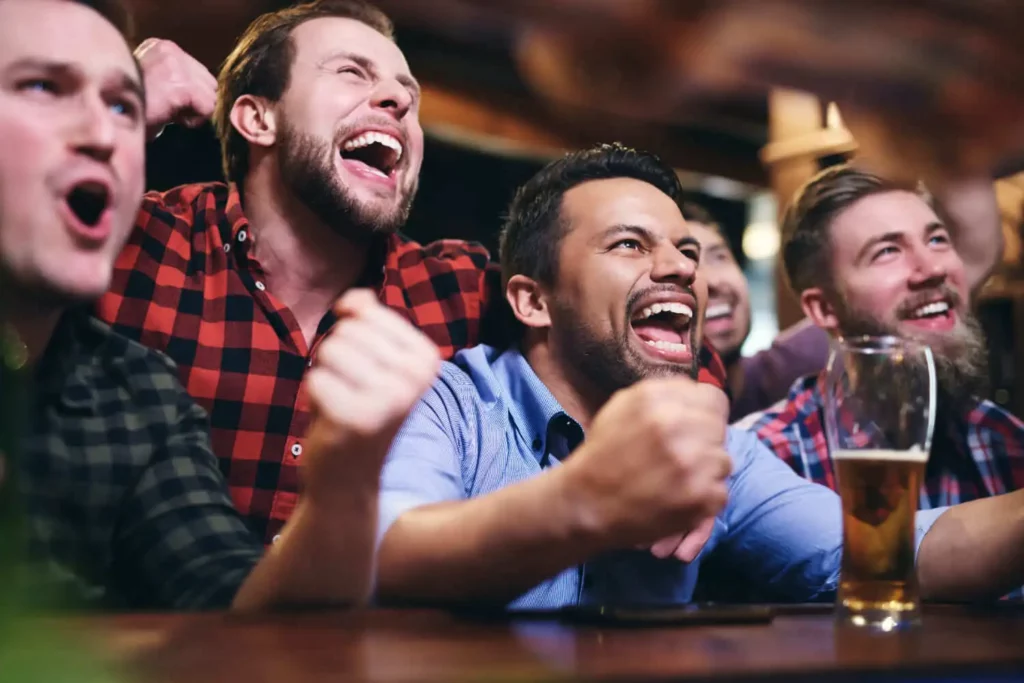  Imagem um grupo de amigos torcendo felizes no balcão de um bar para ilustrar matéria sobre bares com telão