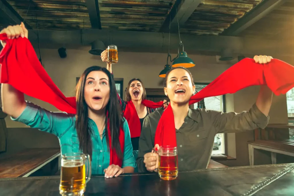 Imagem de três mulheres celebrando em um bar para ilustrar matéria sobre bares para ver jogo