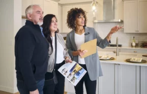 Imagem de um casal formado por um homem e uma mulher visitando um imóvel na companhia de uma corretora imobiliária para ilustrar matéria sobre captação de imóveis