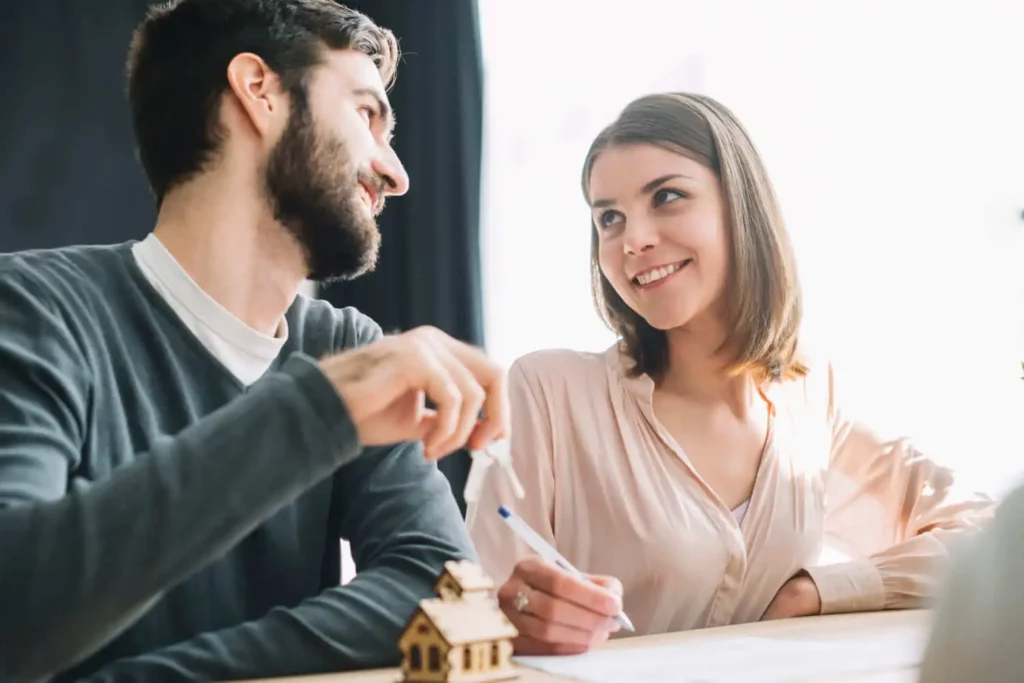 Imagem de um casal casal sorridente se olhando enquanto a mulher assina um documento para ilustrar matéria sobre como financiar apartamento próprio