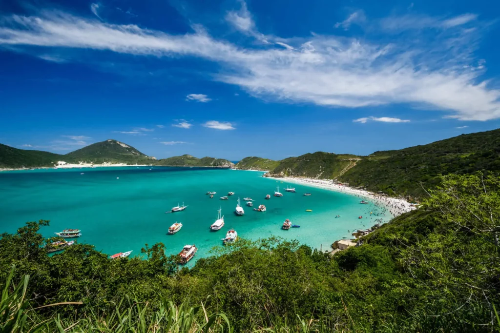 Imagem do Pontal de Atalaia, em Arraial do Cabo, mostra mar com algumas embarcações e vegetação ao redor para ilustrar matéria sobre o interior do Rio de Janeiro