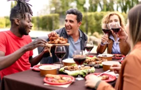 Imagem de um grupo de pessoas sentados ao redor de uma mesa enquanto comem, brindam taças de vinho e se divertem para ilustrar matéria sobre as melhores churrascarias de São Paulo